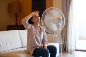 Woman feeling hot and trying to refresh in summertime heat using a fan